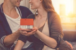 Baufinanzierung: Ein junges Paar hält ein Modellhaus in den Händen