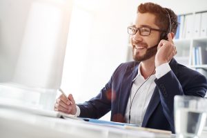 Kontakt: Ein freundlich lächelnder Mitarbeiter mit Headset am Computer